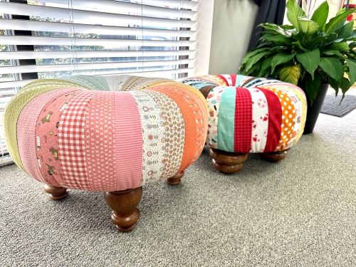 Two colorful patchwork ottomans near blinds.
